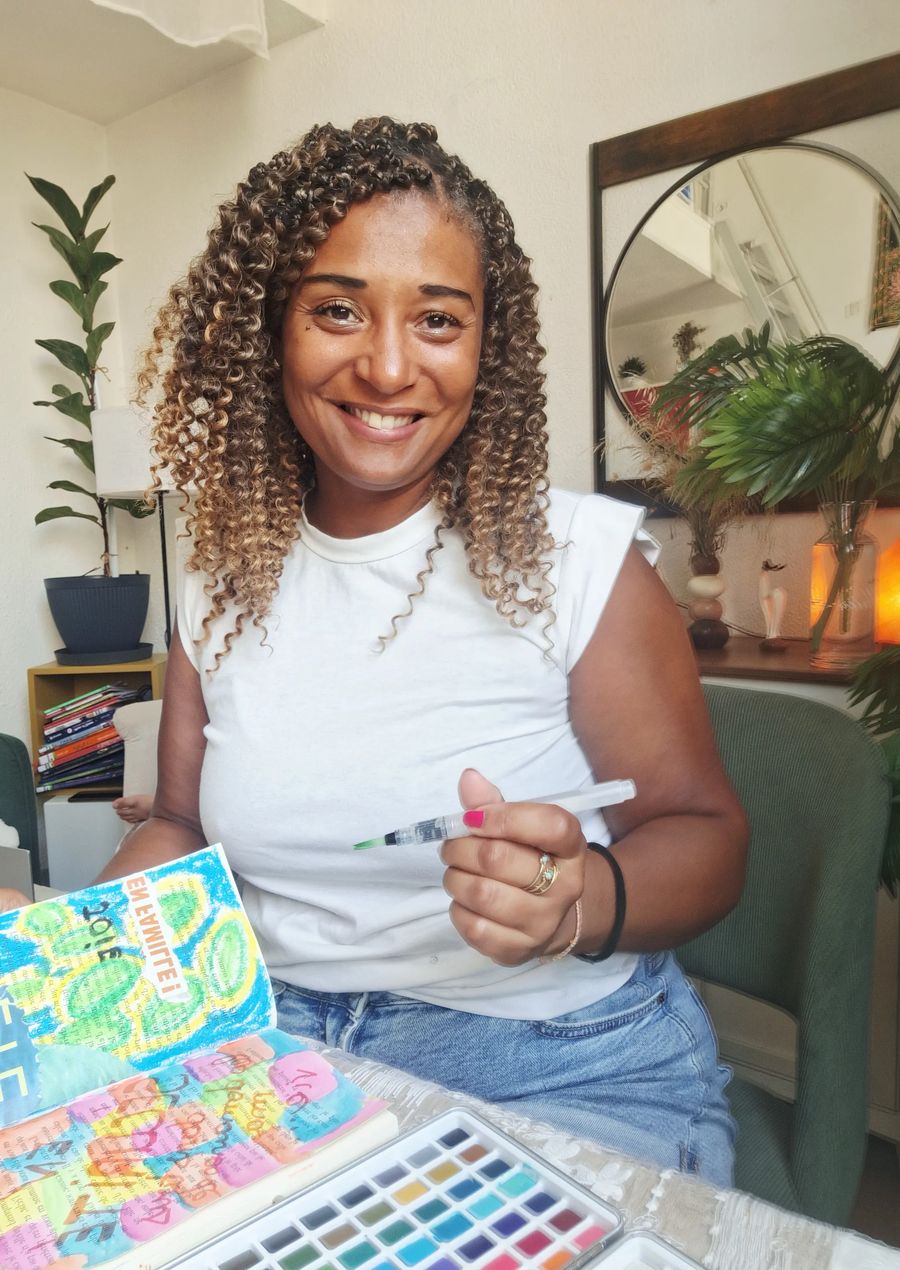 Johanna souriante, pinceau à la main, devant son carnet d'art journaling coloré